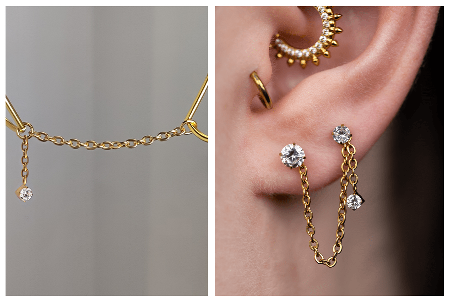 Asymetryczny złoty łańcuszek z małym kryształkiem, pokazany na zbliżeniu oraz założony między dwoma przekłuciami ucha