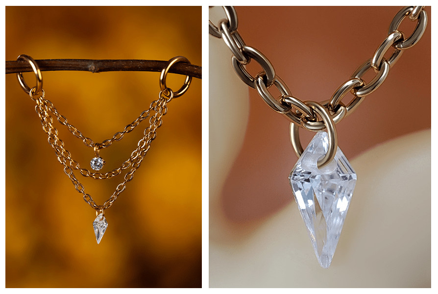 Delikatny potrójny łańcuszek z kryształkami do piercingu – zwisa między dwoma kolczykami kółkami na gałązce oraz w zbliżeniu na podłużny, przeźroczysty kryształ