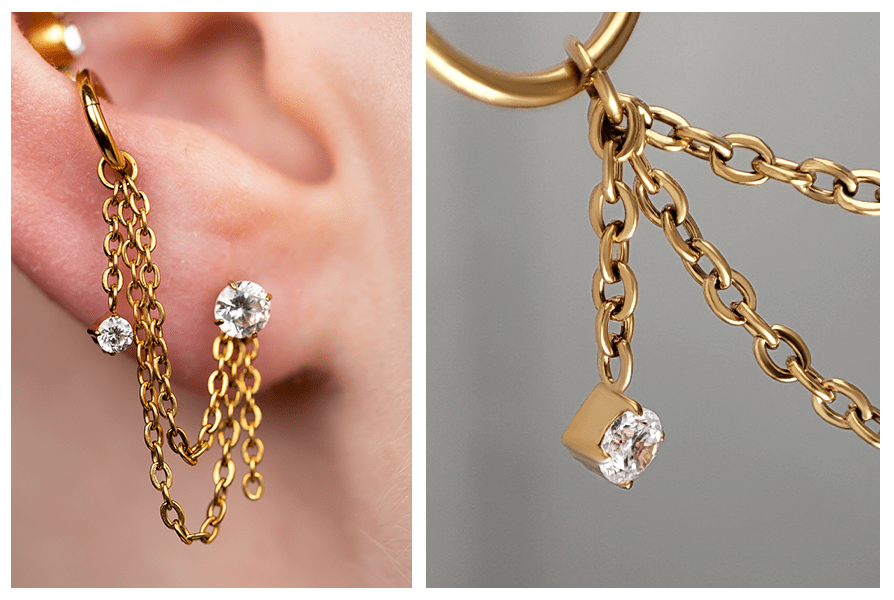Zbliżenie na złoty łańcuszek symetryczny z kryształkiem doczepiony do kółka, zwisający obok dwóch kolczyków w płatku ucha