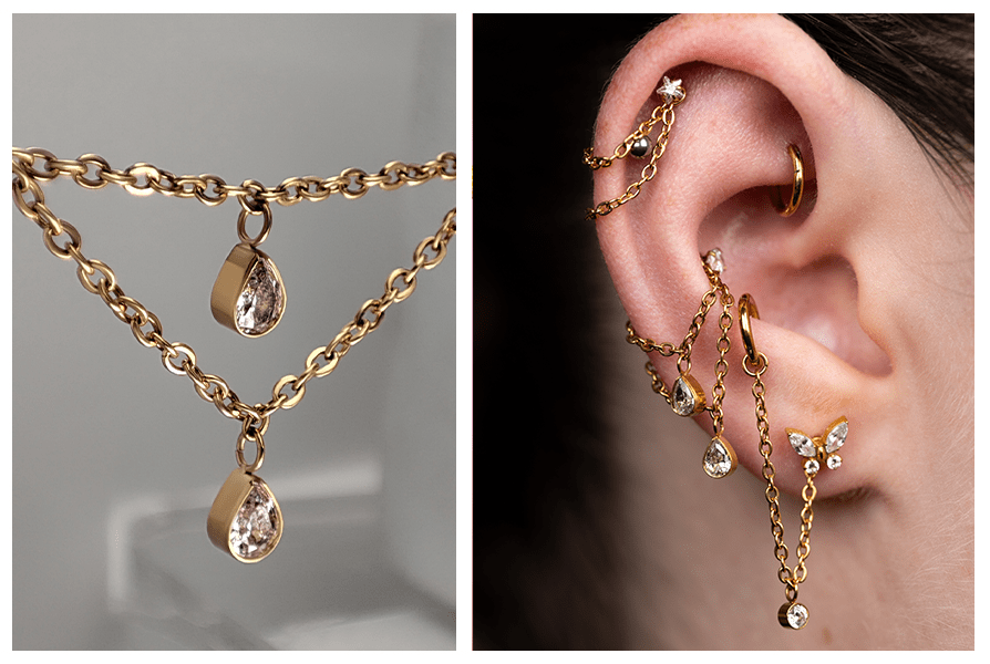 Złoty podwójny łańcuszek z dwiema kryształowymi łezkami, pokazany w zbliżeniu oraz założony na uchu z kilkoma przekłuciami jako dodatek do kolczyków