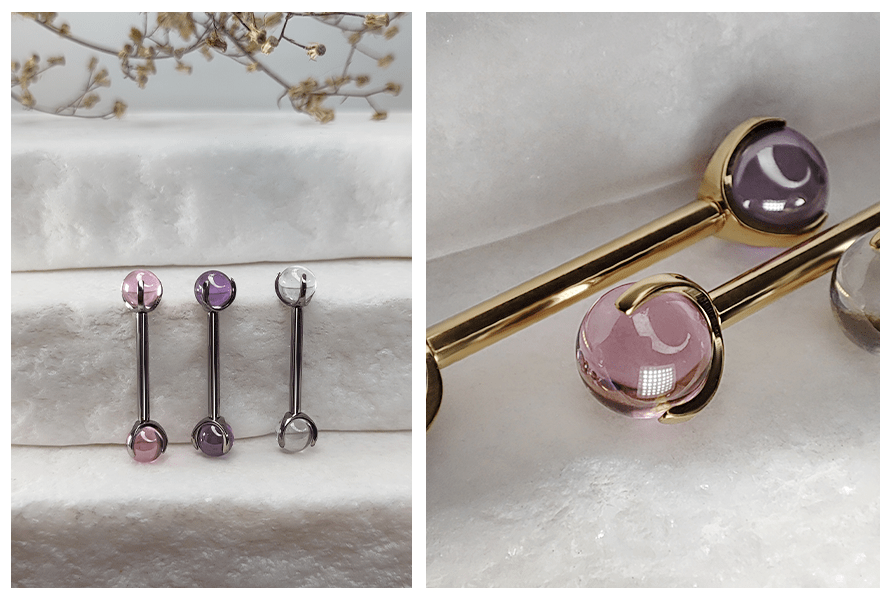 Trzy proste sztangi do piercingu z przezroczystymi kulkami w różu, fiolecie i bezbarwnym kolorze na kamiennym tle, w ujęciu pełnym i zbliżeniu