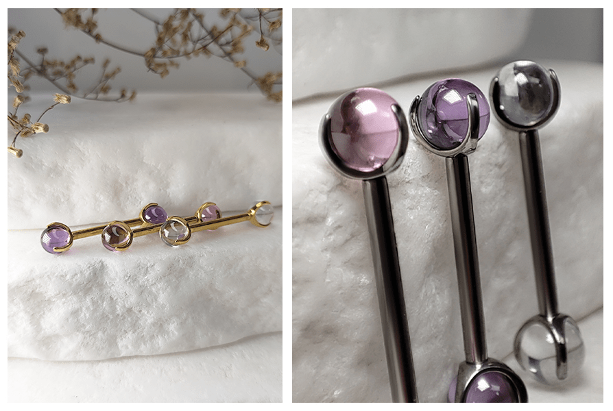 Złote i stalowe sztangi do piercingu z przezroczystymi kulkami w różnych kolorach, pokazane na jasnym kamieniu w ujęciu z daleka i detalu