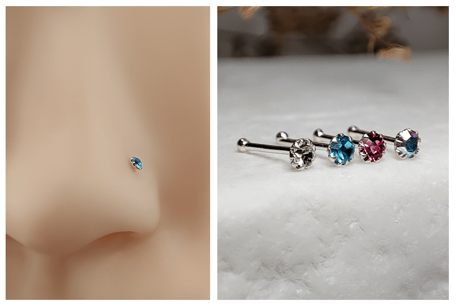 Prosty kolczyk do nosa z niebieskim kryształem w silikonowym nosie manekina oraz rząd srebrnych kolczyków do nosa z kolorowymi kryształami ułożonych na białym kamieniu