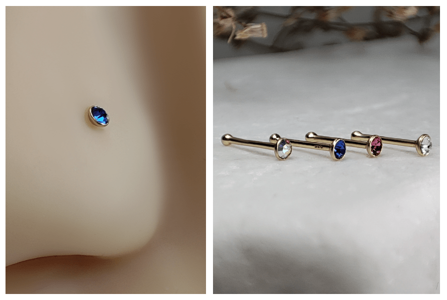 Prosty kolczyk do nosa z niebieskim okrągłym kryształkiem w złotej oprawie w silikonowym nosie oraz rząd złotych kolczyków z kolorowymi kryształkami ułożonych na białym kamieniu