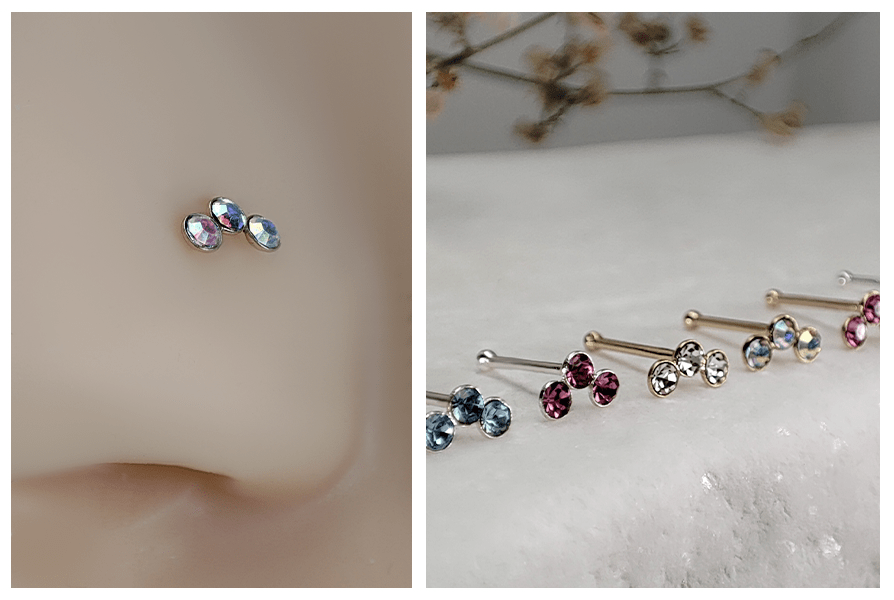 Prosty kolczyk do nosa z trzema jasnymi kryształkami założony w skrzydełku nosa oraz rząd kolczyków do nosa z potrójnymi kryształkami w kilku kolorach na białym kamieniu