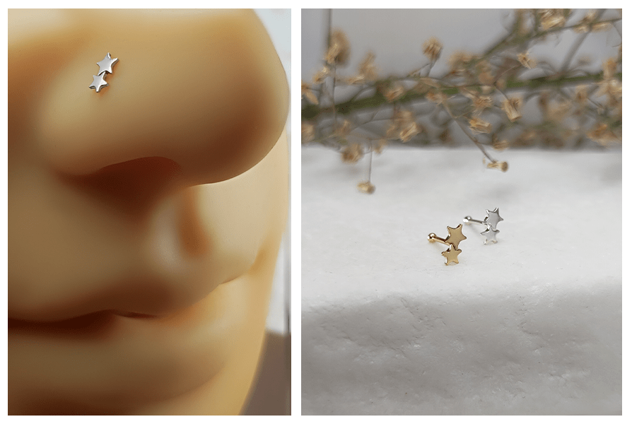 Prosty kolczyk do nosa z małymi srebrnymi gwiazdkami w nosie oraz dwa kolczyki z gwiazdkami w kolorze złotym i srebrnym ułożone na białym kamiennym tle
