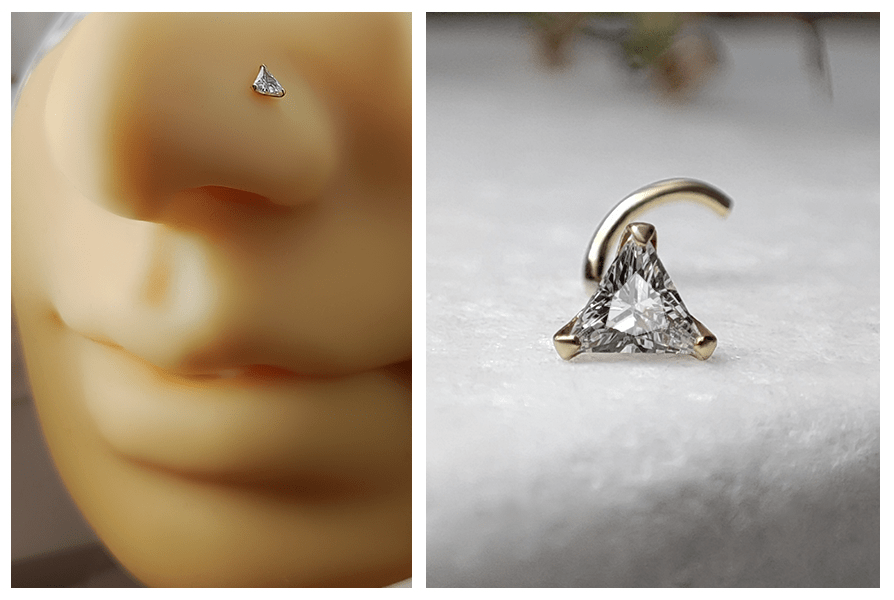 Delikatny zakręcony kolczyk do nosa z małym trójkątnym kryształem założony w skrzydełku nosa oraz detal pojedynczego kolczyka leżącego na białym kamieniu