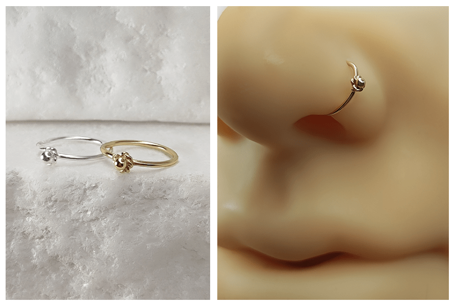 Rozginane kółko (srebro 925) z małym kwiatuszkiem w złotym i srebrnym kolorze, pokazane na kamiennym tle i założone w silikonowym płatku nosa