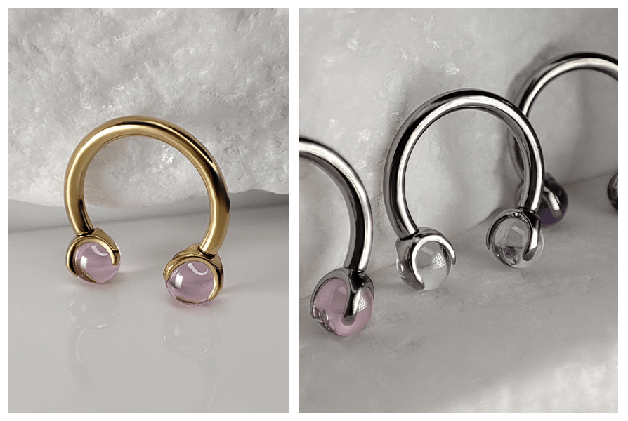 Złota i stalowa podkówka do piercingu z przezroczystymi kulkami, pokazane pojedynczo i w zbliżeniu na jasnym tle