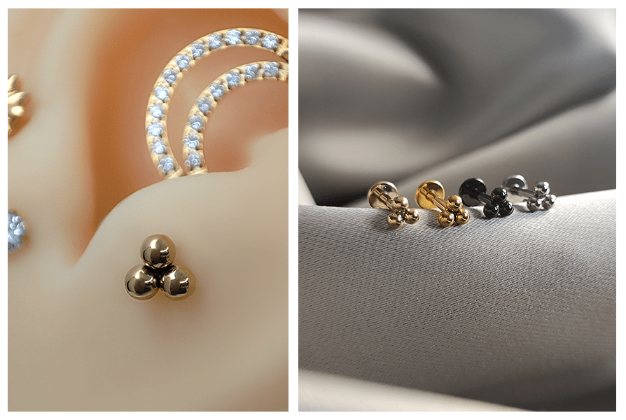 Zbliżenie: złoty labret z trzema kuleczkami w uchu przy podwójnym kółku z kryształkami; po prawej złoty, czarny i srebrny model na tkaninie