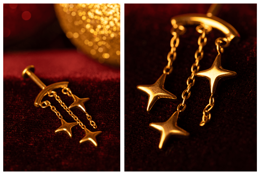 Kolczyk w kolorze złota z trzema gwiazdkami na łańcuszkach sfotografowany na czerwonym tle oraz makro detalu pokazujące gwiazdki i ogniwa łańcuszków (labret do vertical helix)