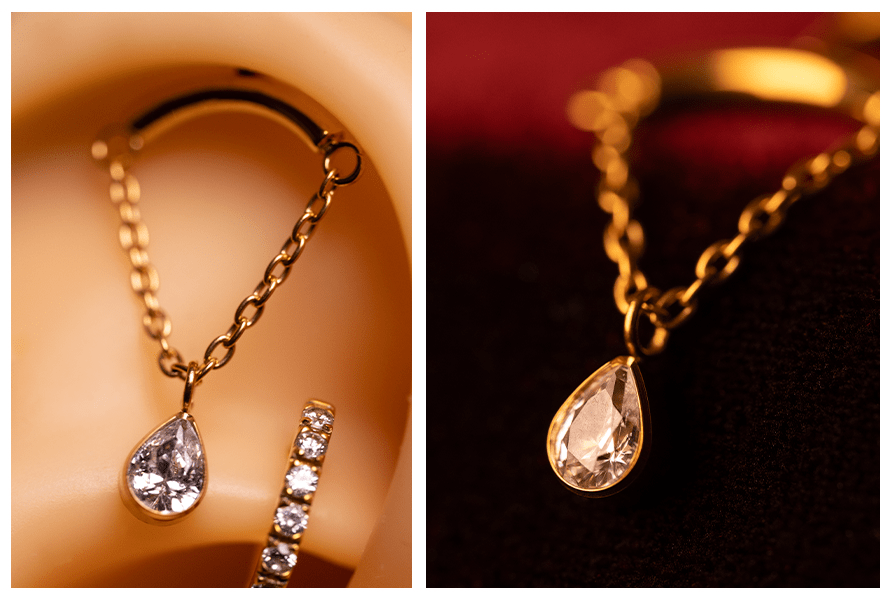 Zbliżenie na labret do vertical helix: gładka belka, łańcuszek i łezka z kryształem przy uchu – obok makro zawieszki łezki na łańcuszku na ciemnoczerwonym tle