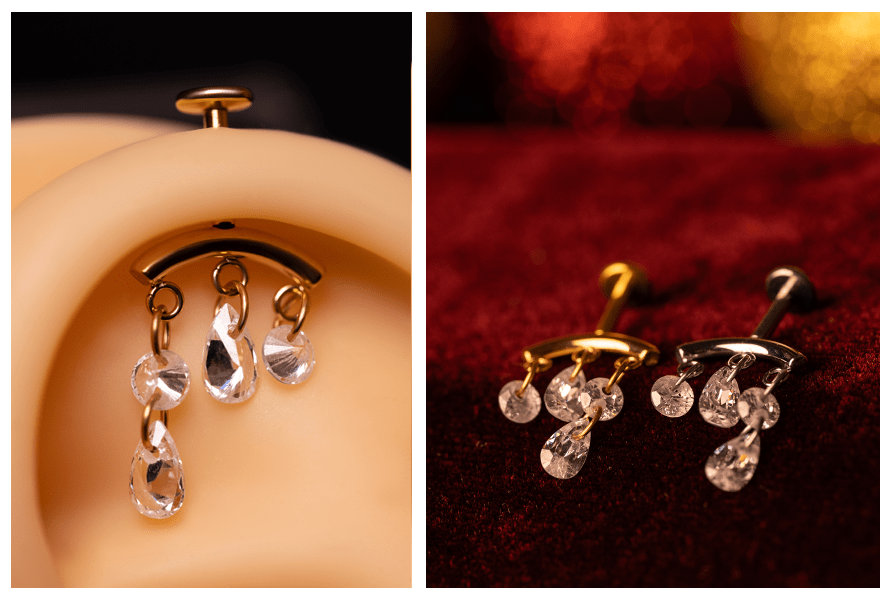 Zbliżenie na kolczyk w uchu z czterema drobnymi kryształkami na kółeczkach – obok dwa labrety (złoty i srebrny) z wiszącymi kryształkami na czerwonym tle