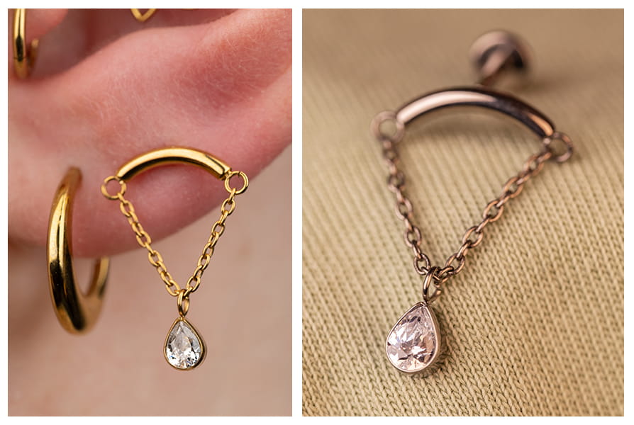 Zbliżenie na złoty labret z łańcuszkiem i wiszącą cyrkonią w kształcie łezki, noszony w uchu obok klasycznego kółka