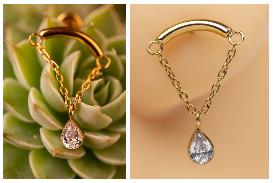 Złoty labret z łańcuszkiem zakończonym cyrkonią w kształcie łezki, pokazany na tle rośliny oraz na silikonowym modelu ucha