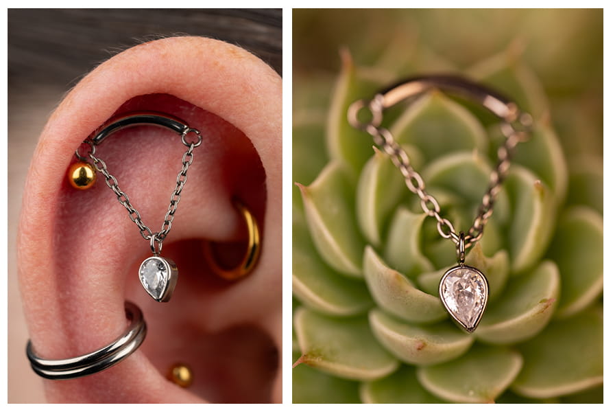 Zbliżenie na labret z delikatnym łańcuszkiem i wiszącą cyrkoniową odwróconą łezką, noszony w górnej części ucha