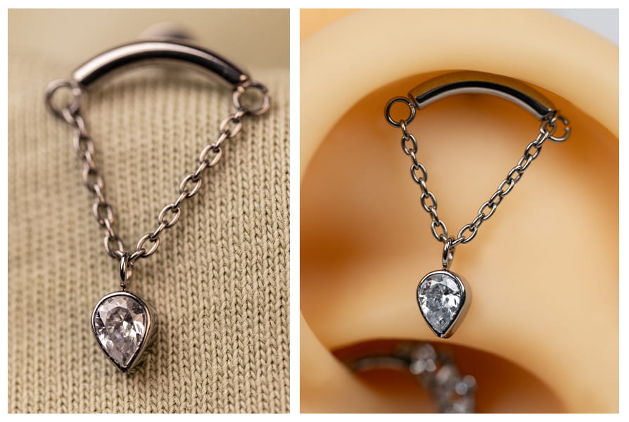 Labret z łańcuszkiem i cyrkoniową odwróconą łezką sfotografowany na jasnym tle, na tle sukulenta oraz na modelu ucha