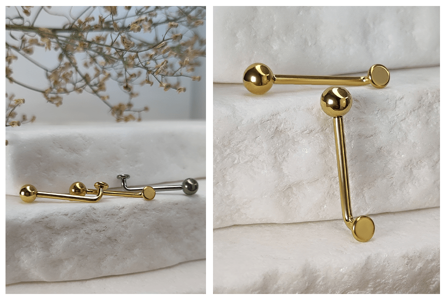 Złoty i srebrny kolczyk intymny Christina w formie L-bar z kulką i płaskim dyskiem, pokazany na jasnym kamiennym tle w dwóch ujęciach – kilka sztuk ułożonych poziomo oraz zbliżenie na złoty model